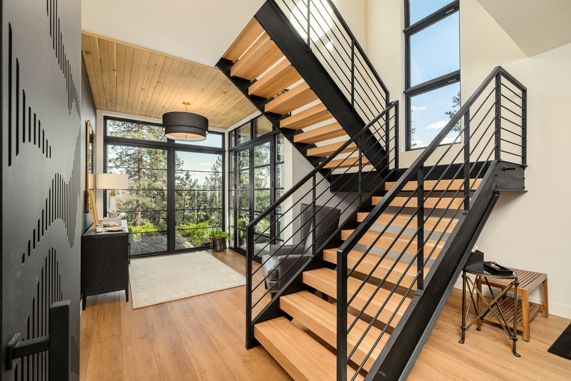 Open-riser wood stair with black steel railings and full-height windows