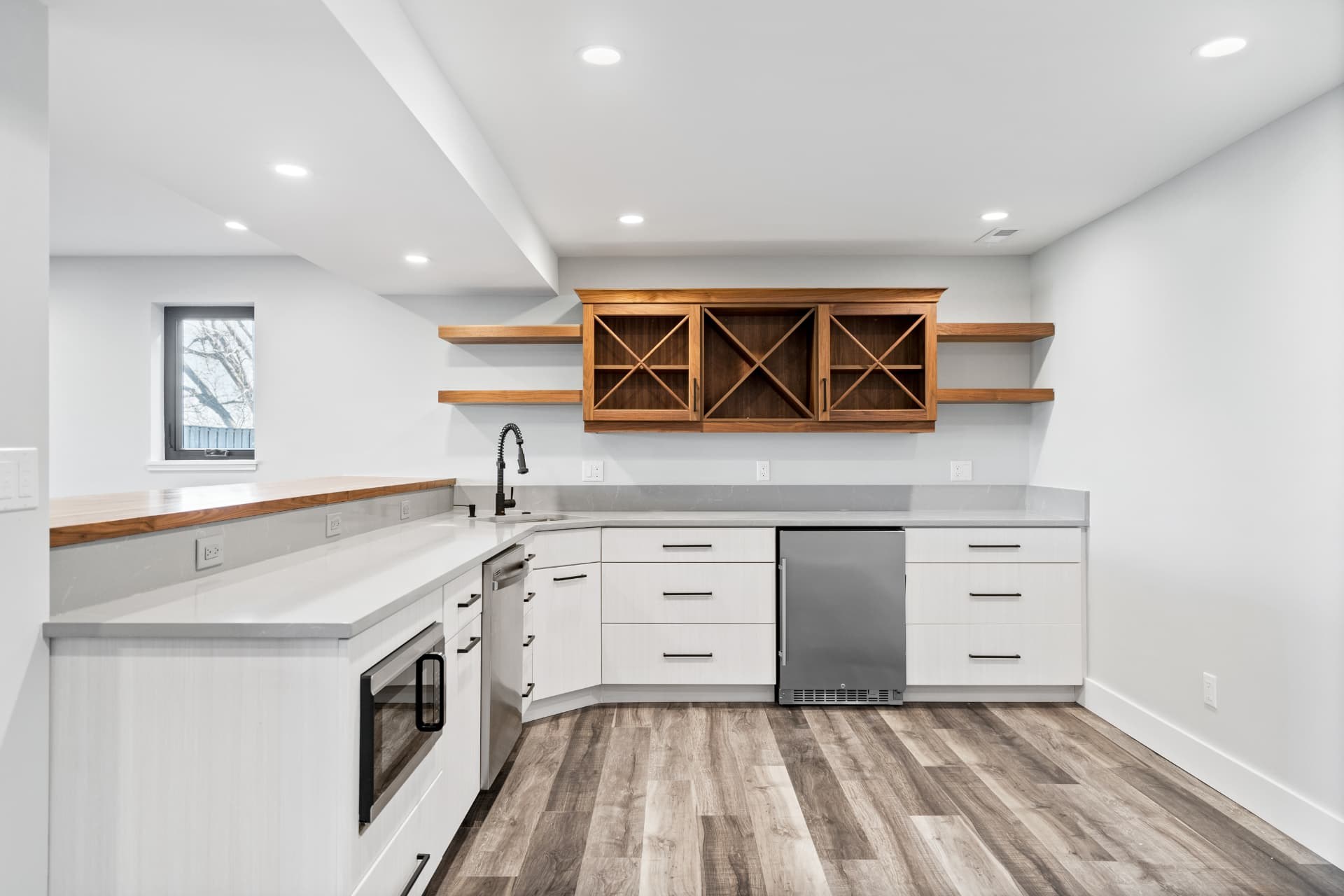 Lower-level kitchenette with white cabinetry and a walnut wine rack