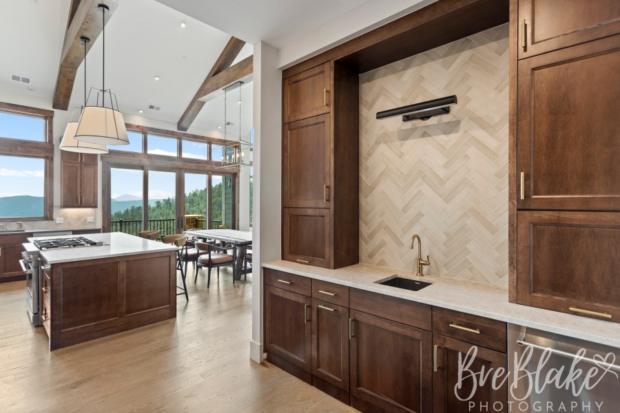 Built-in bar with herringbone tile and dark wood cabinetry beside the vaulted kitchen