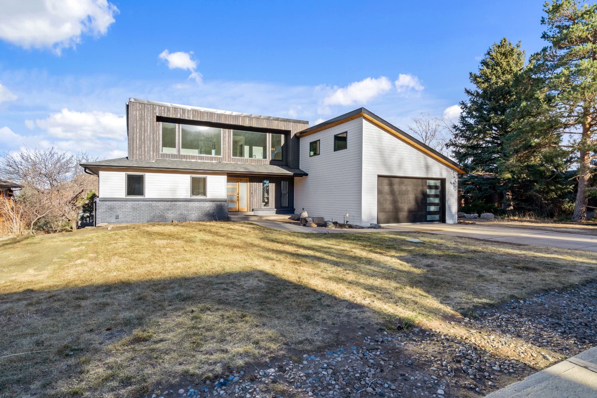 Front elevation of the finished pop-top remodel in Golden, with white siding, weathered vertical wood cladding and a dark garage door