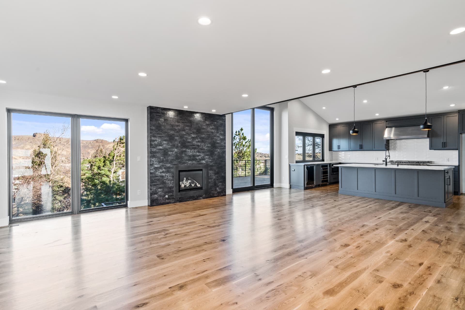 Open living room with a dark tile fireplace wall, white oak floors and the kitchen beyond