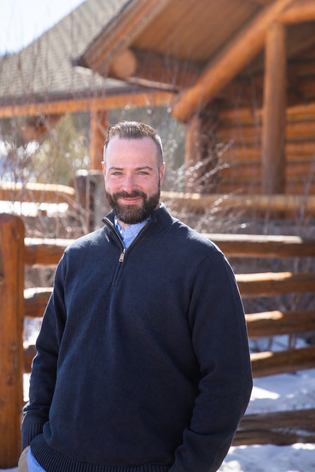 Matt Laffey smiling in a navy sweater outside a log home in winter