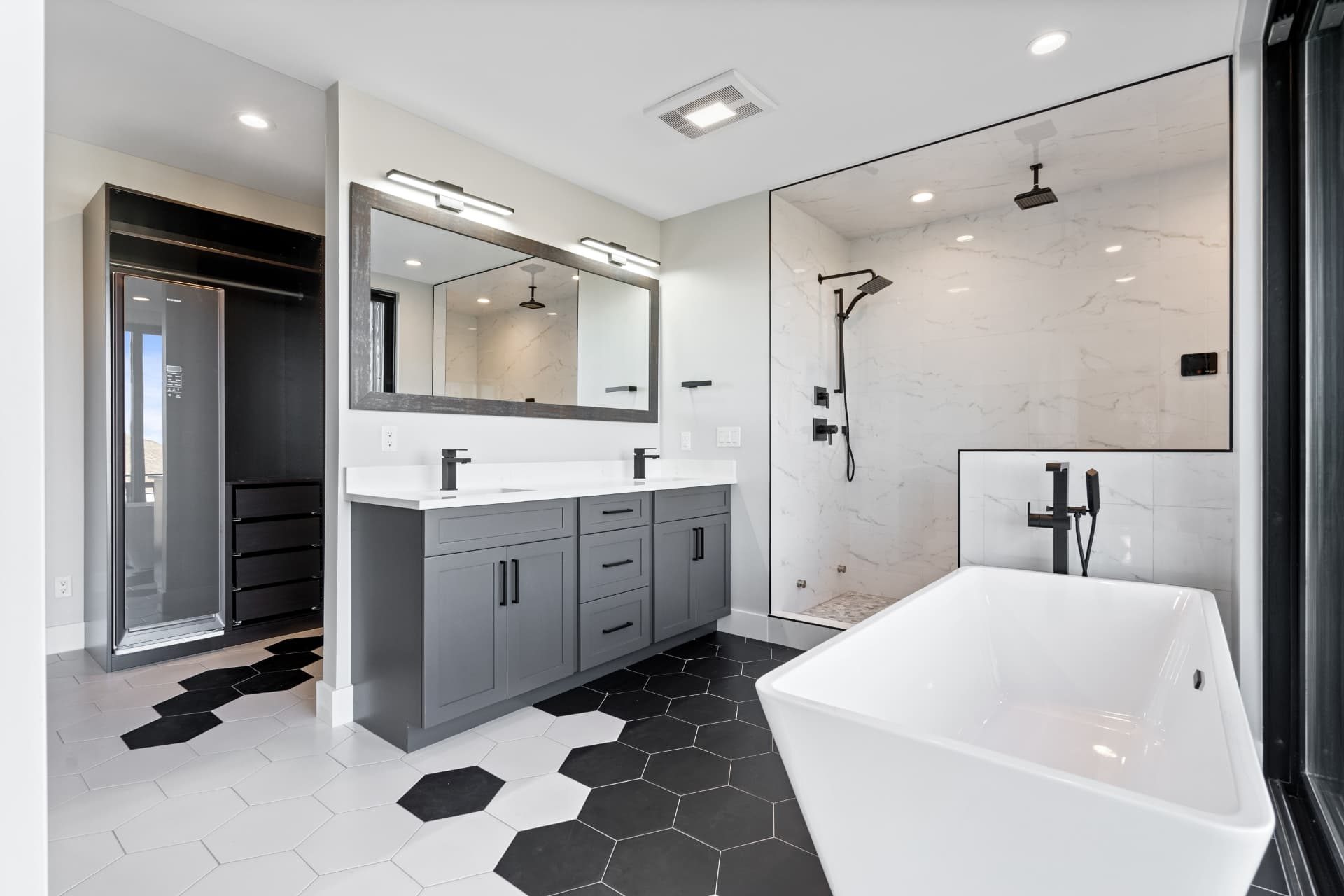 Primary bathroom with grey vanity, marble shower, freestanding tub and hex tile floor