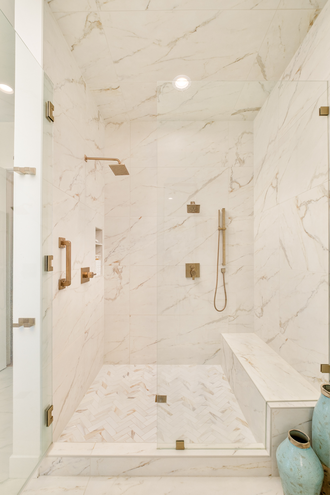 Walk-in marble shower with brass fixtures and a built-in bench
