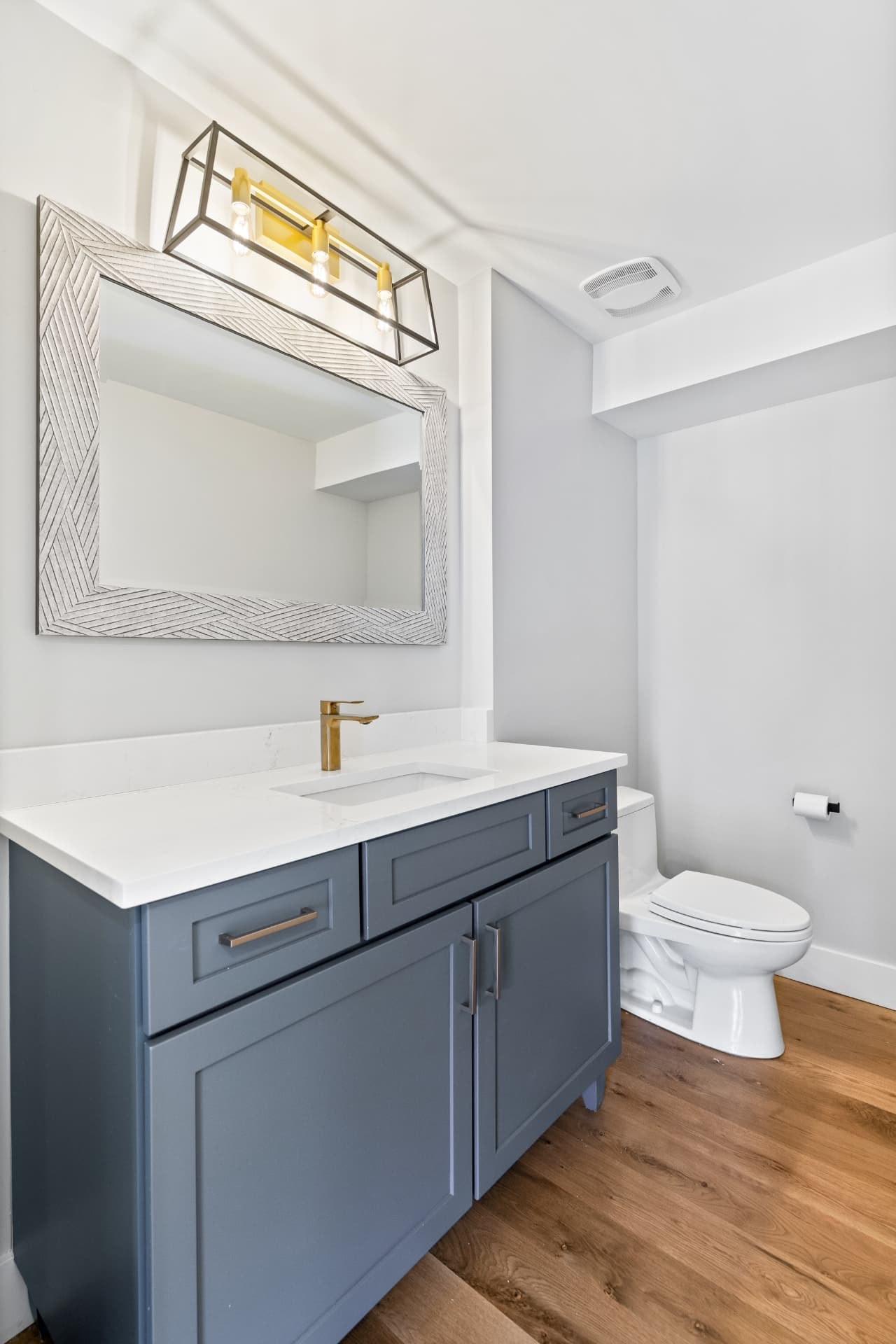Bathroom vanity with a patterned mirror and gold light fixture
