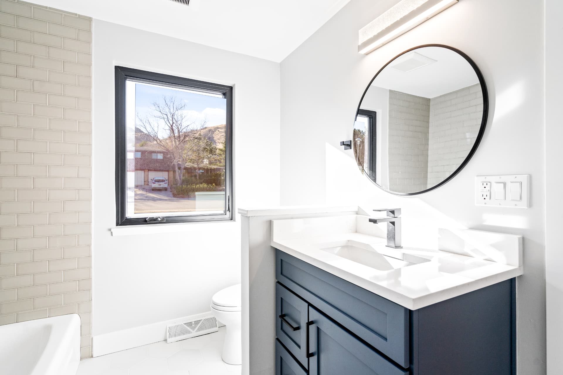 Guest bathroom vanity in navy cabinetry with a round black mirror