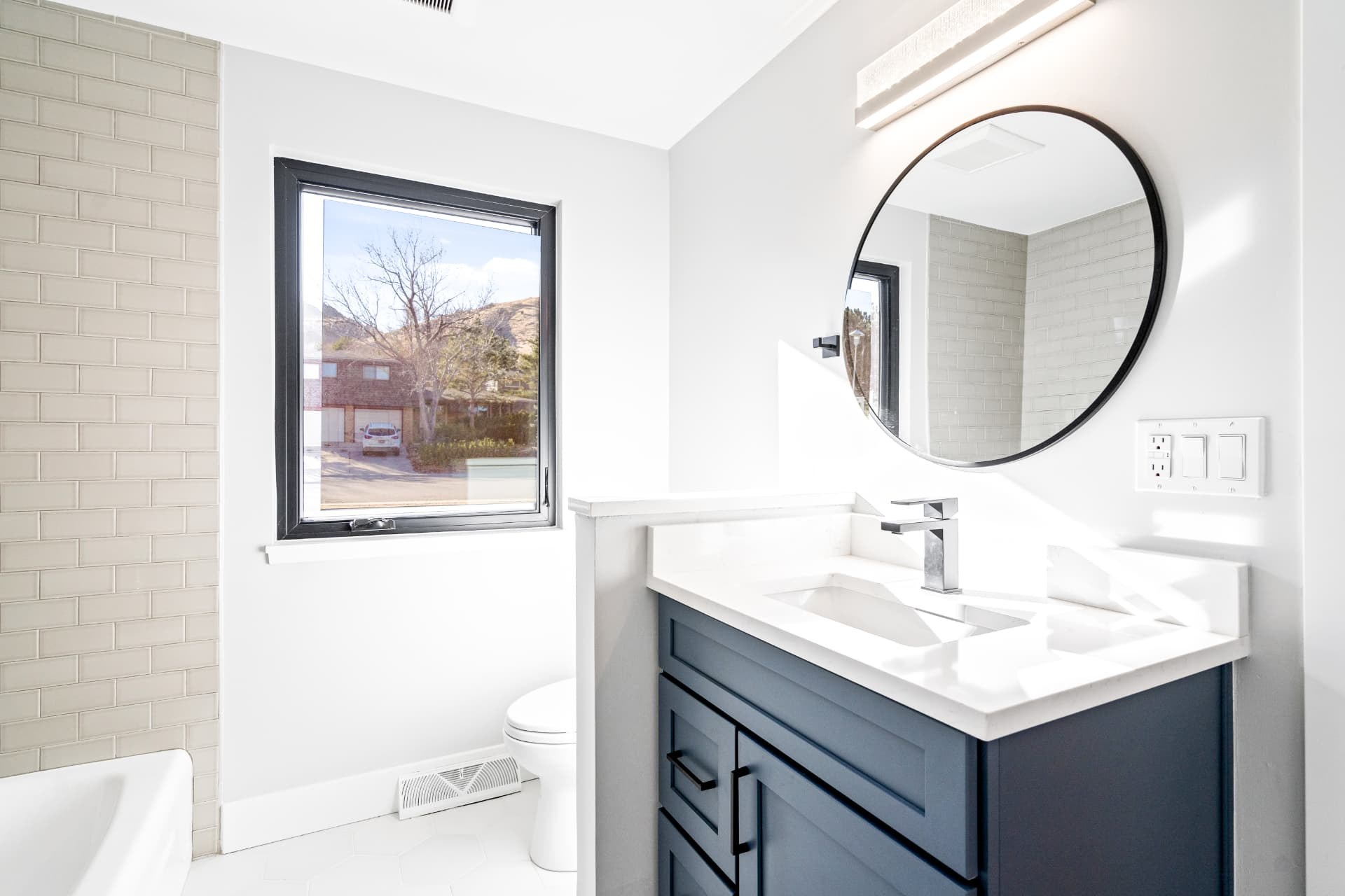 Bathroom vanity with a round mirror beside a black-framed window