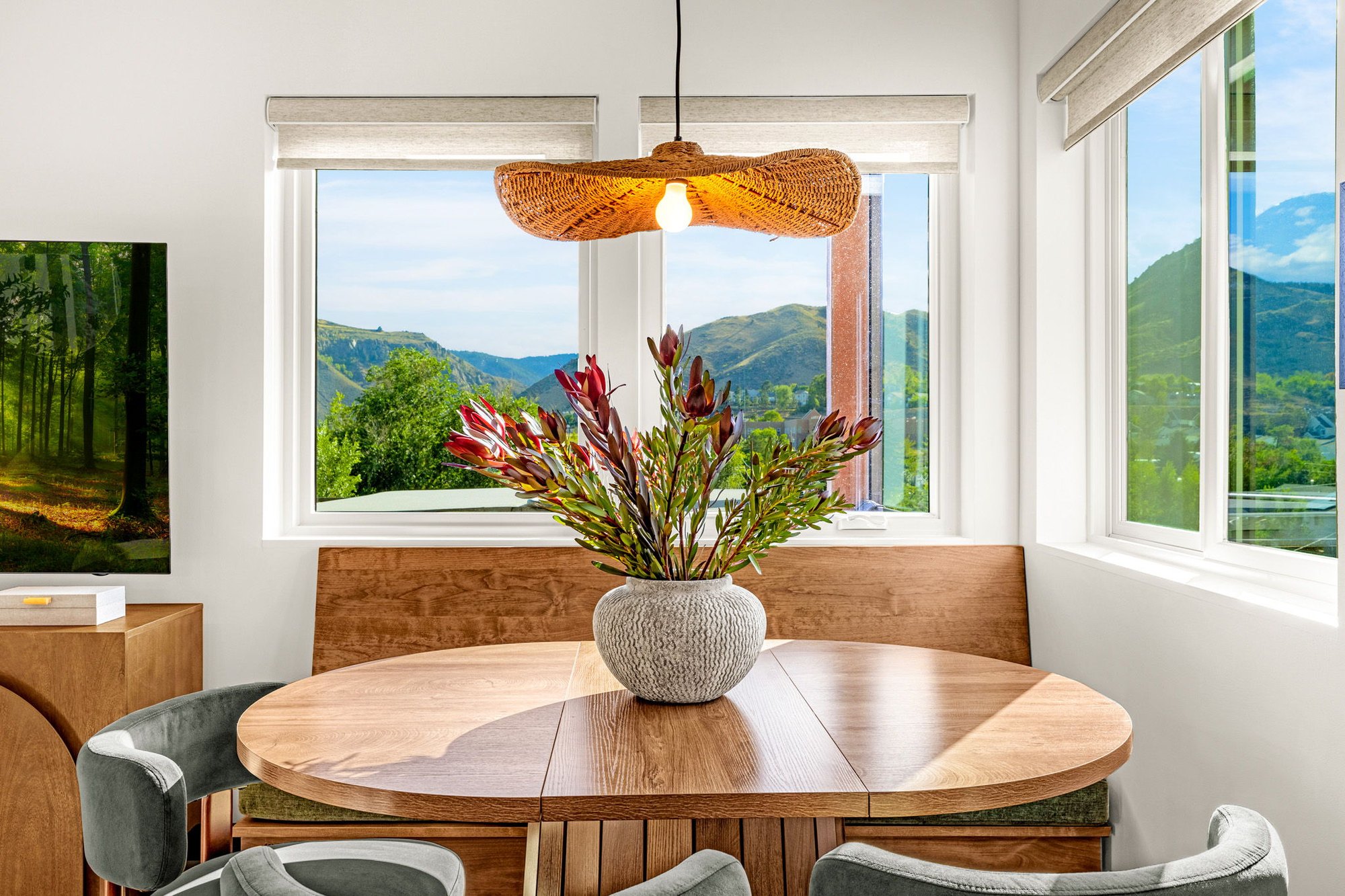 Round dining table beneath a woven pendant with a foothills view