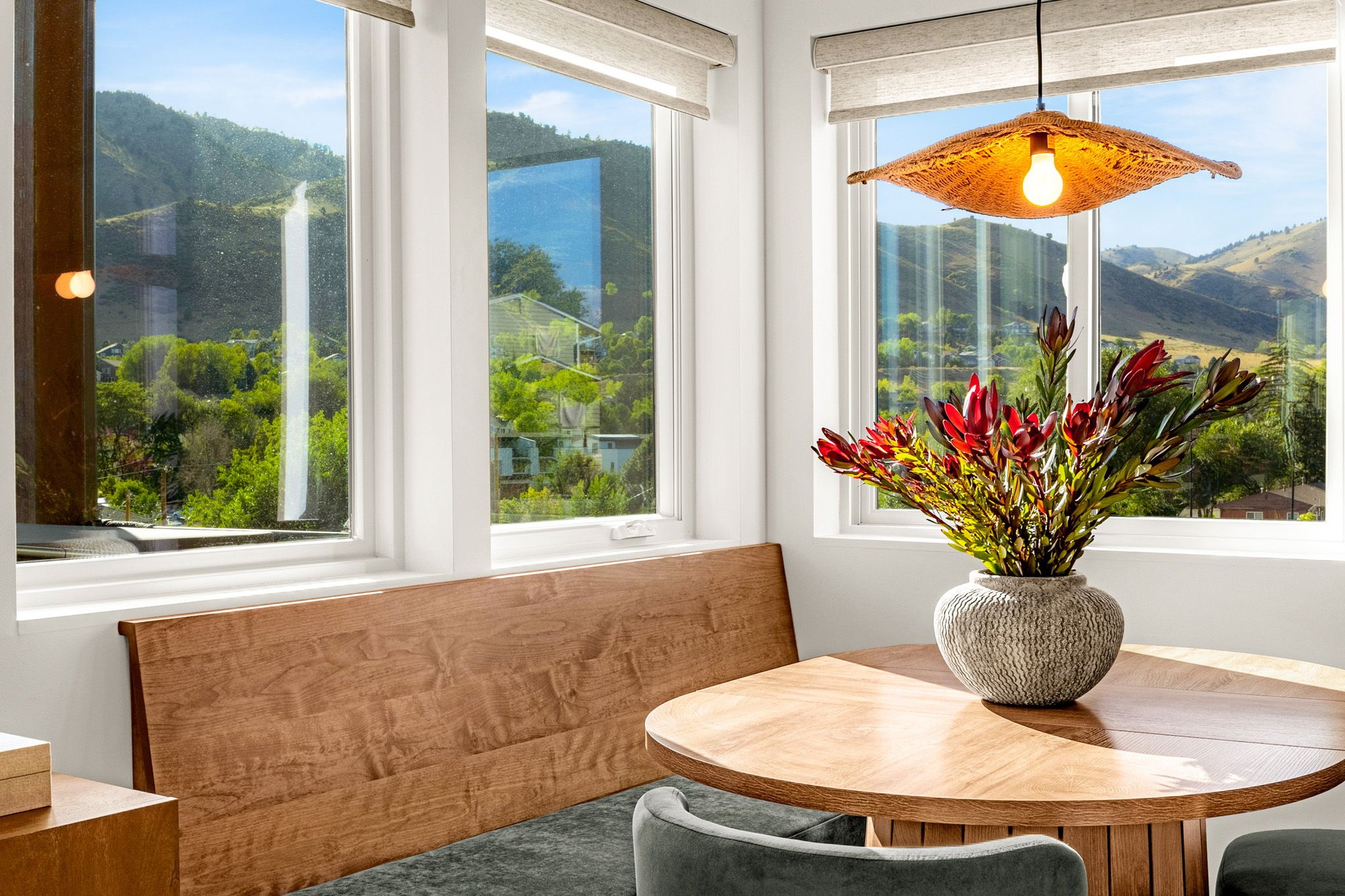 Built-in walnut banquette and round dining table beneath a corner window