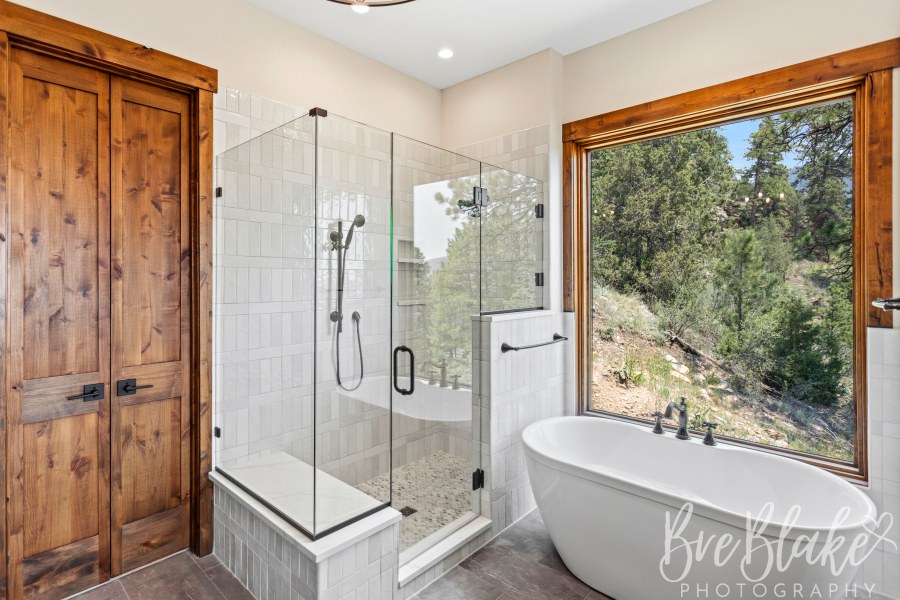 Primary bath with a glass shower, freestanding tub and large picture window to the trees